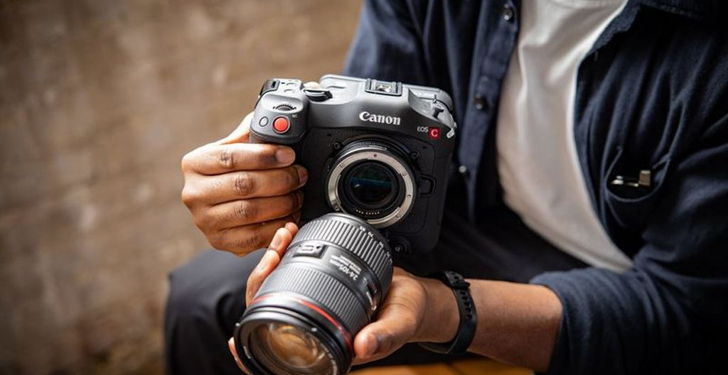 Vue de dos d'un photographe dont les mains attachent une bague d'adaptation à un boîtier mirrorless, action en gros plan sur un plan de travail moderne